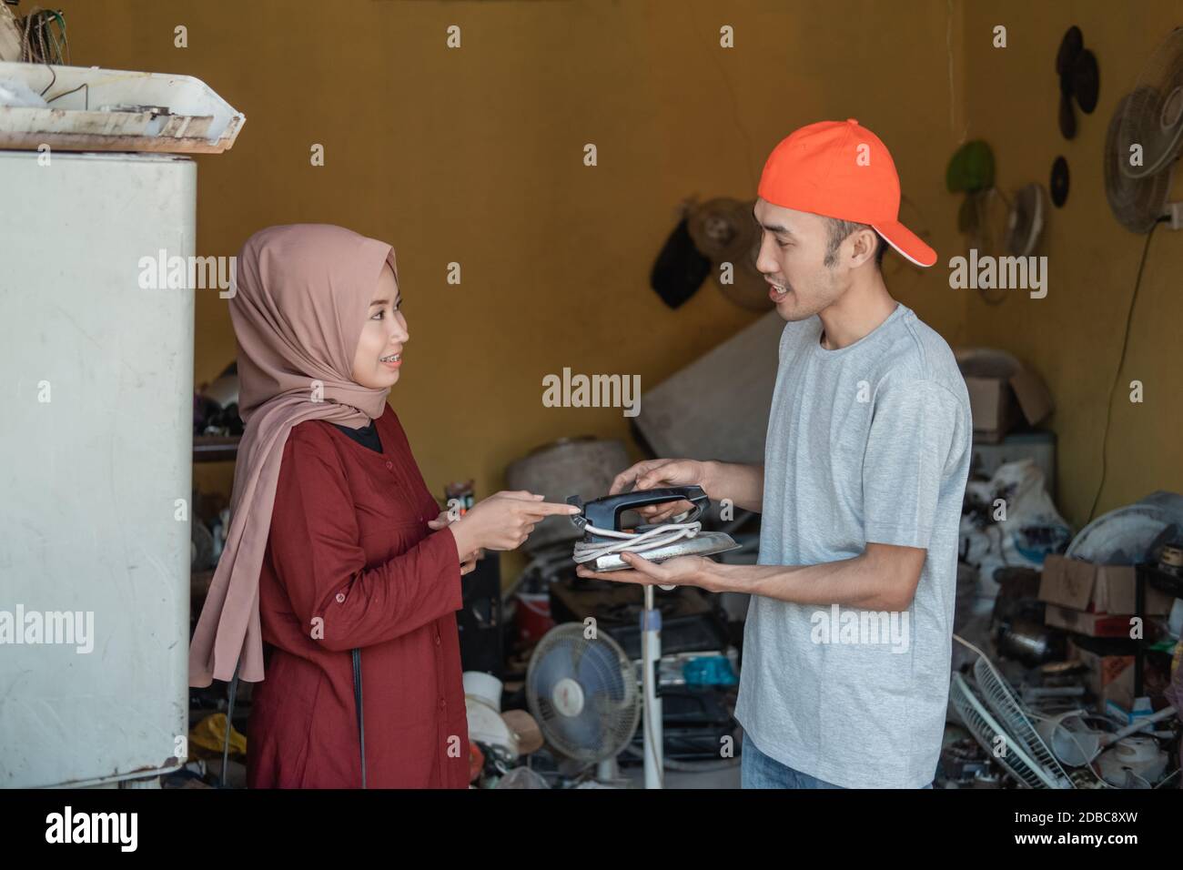 hijab woman takes a broken iron to an electronics repairman at an electronics repair shop Stock Photo