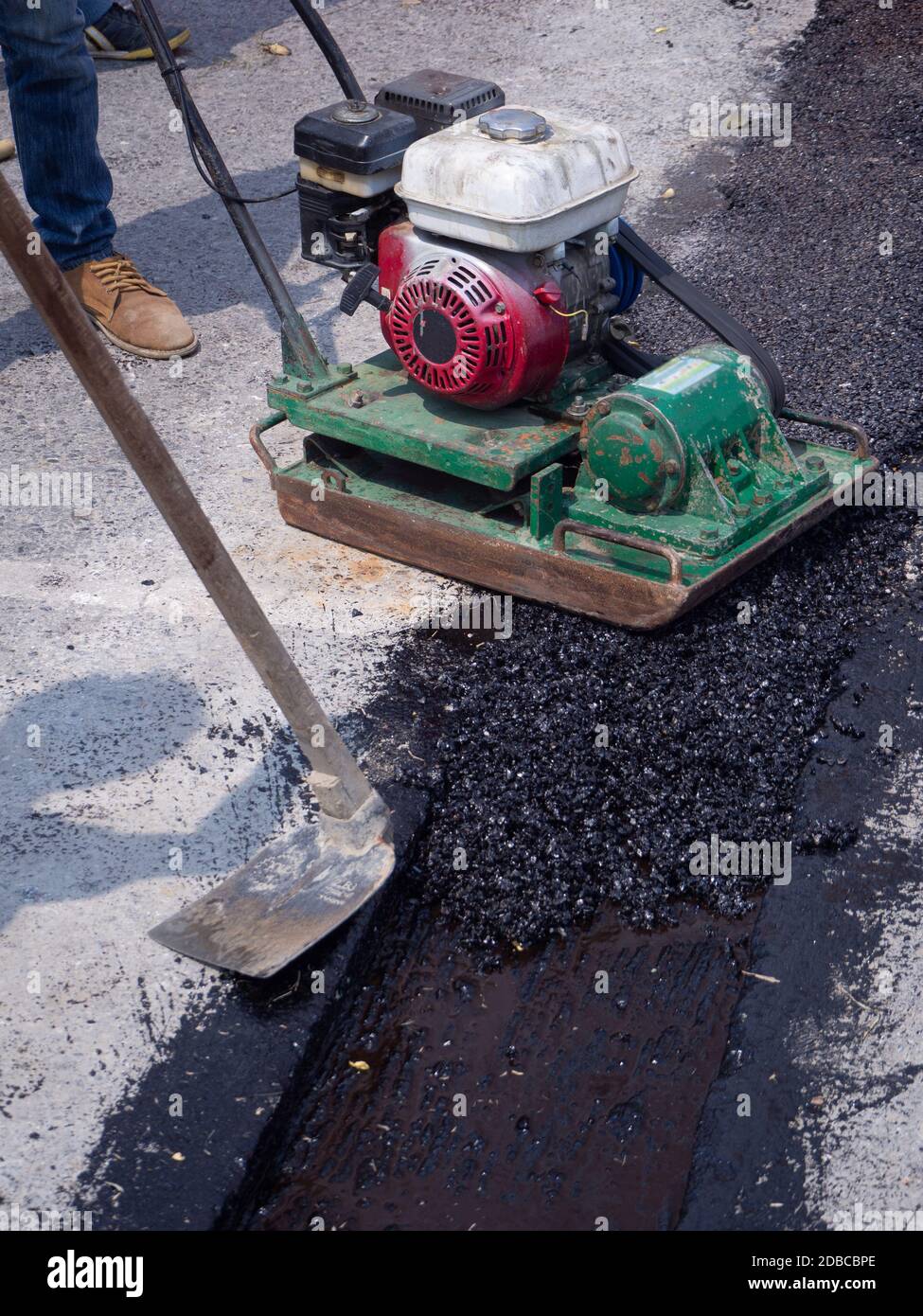 Worker use vibratory plate compactor compacting asphalt at road repair