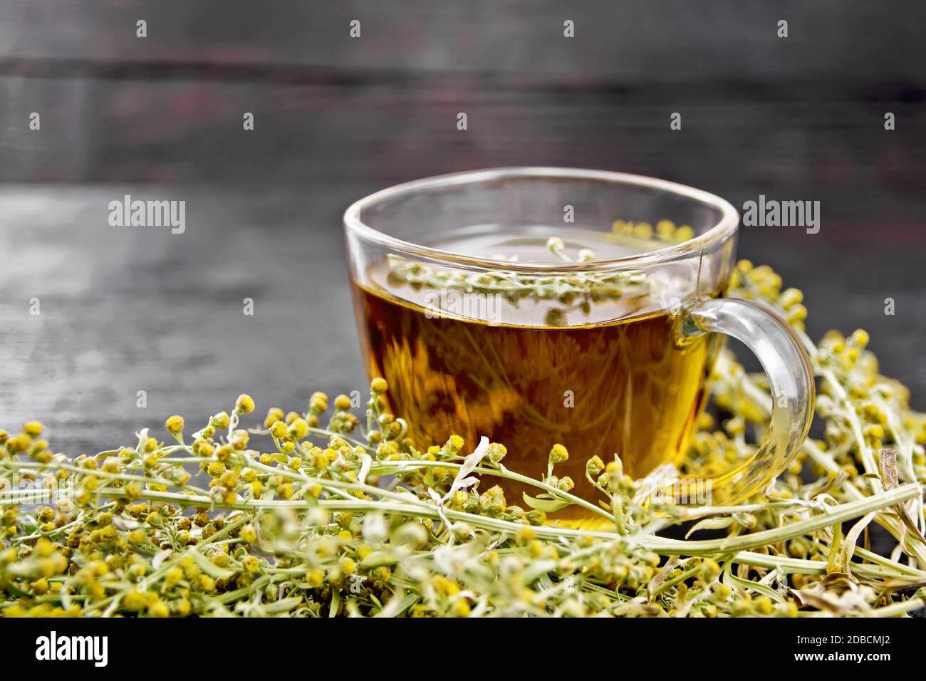 Gray wormwood herbal tea in a glass cup, fresh sagebrush flowers on wooden board background Stock Photo