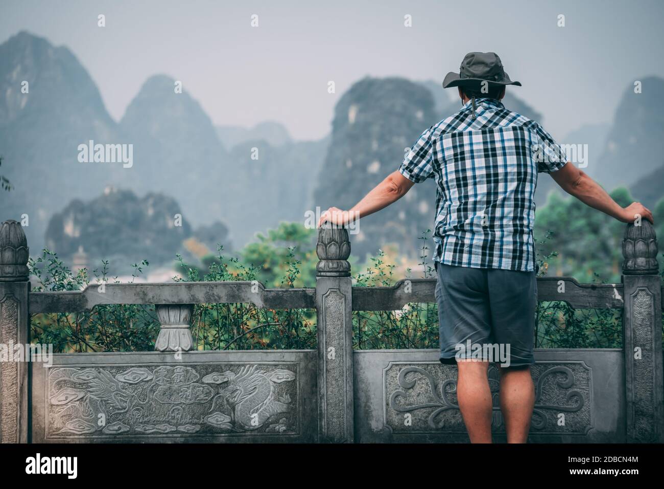 A view of a male laying on the fence and enjoying the beautiful view of the karst mountains in Yangshuo in the morning Stock Photo