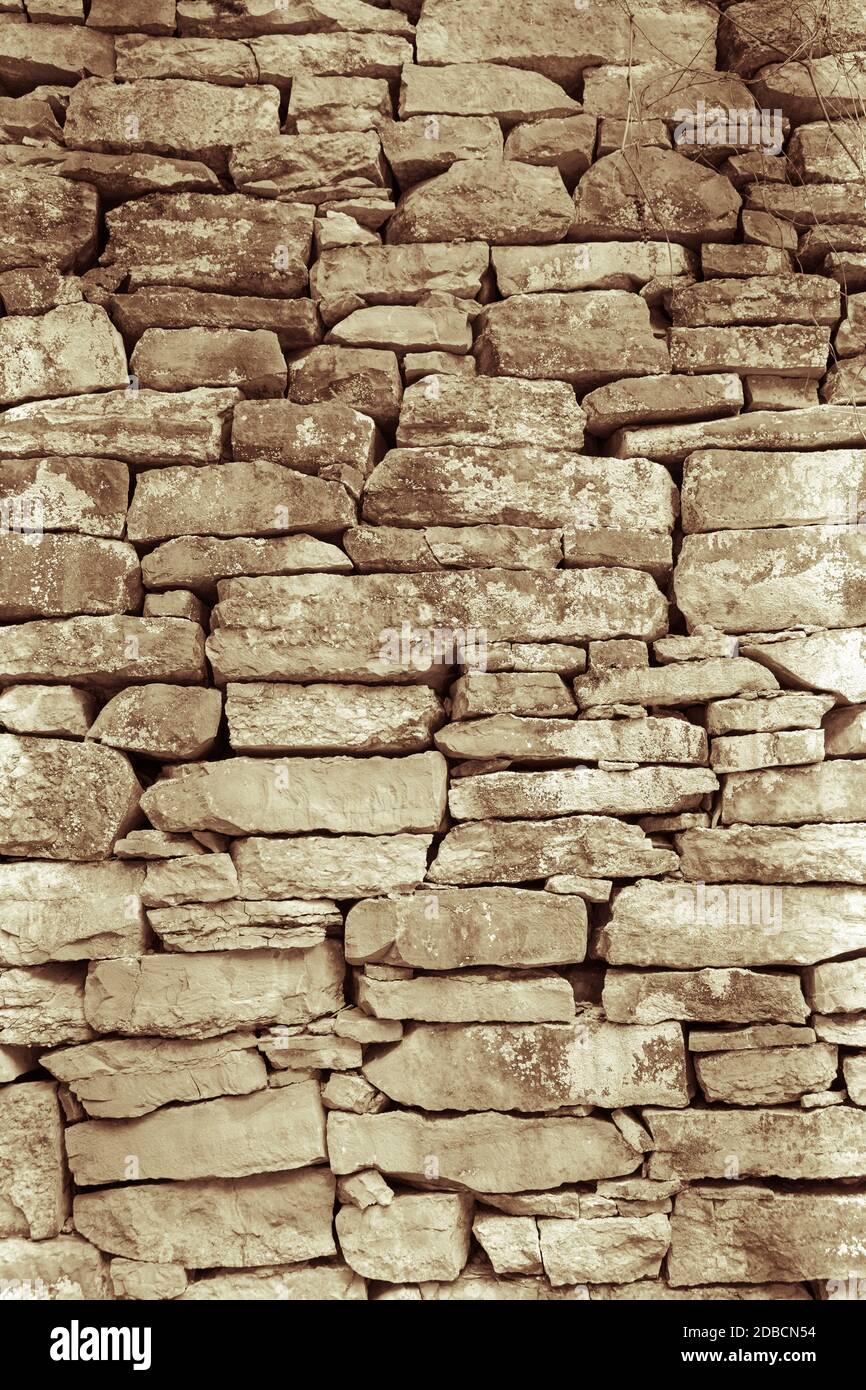 A vertical greyscale shot of an old wall made with uneven sizes of rocks Stock Photo