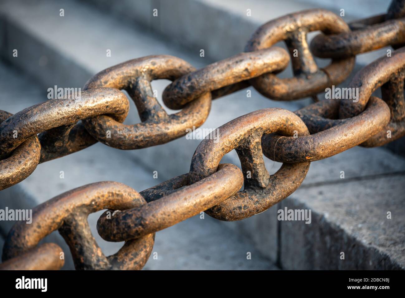 A closeup selective focus shot of two parallel thick steel chains with a blurry background of stone stairs Stock Photo
