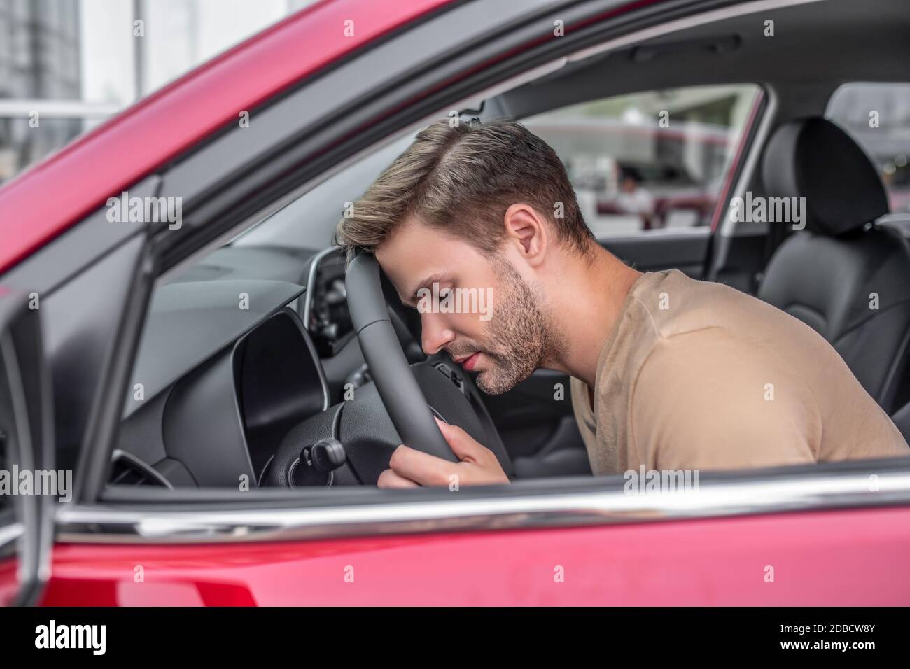 Tired young male resting his head on steering wheel Stock Photo
