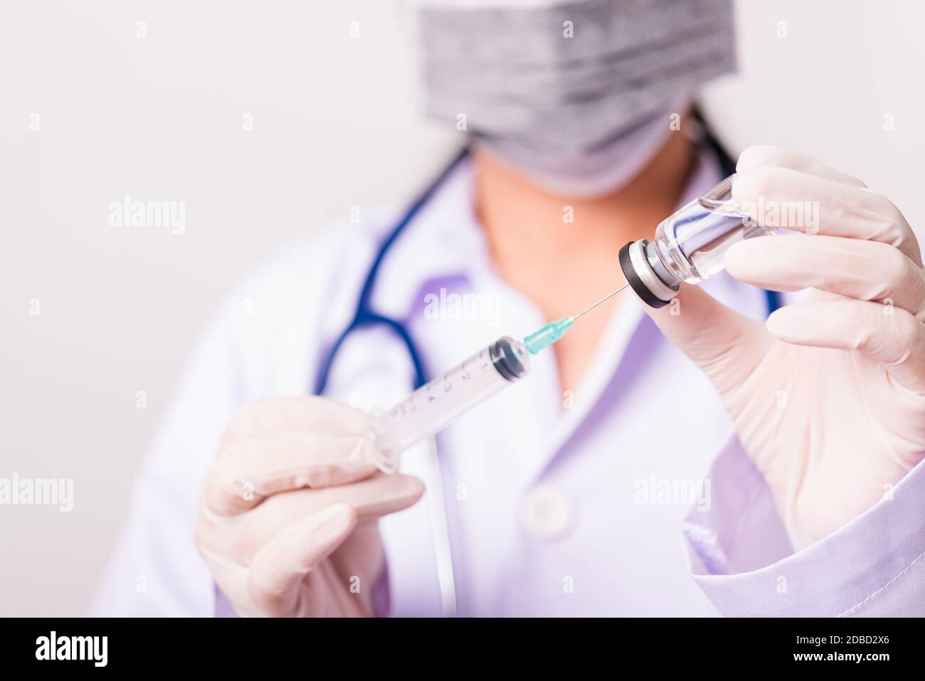 Closeup female woman doctor, nurse or scientist in uniform wearing face mask protective in lab use holding and syringe injecting to vial vaccine bottl Stock Photo