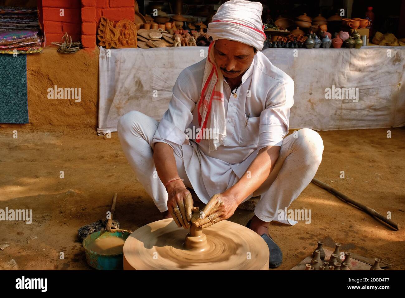 Indian potter at work: throwing the potter's wheel and shaping ceramic vessel and clay ware: pot, jar in pottery workshop. Experienced master. Handwor Stock Photo