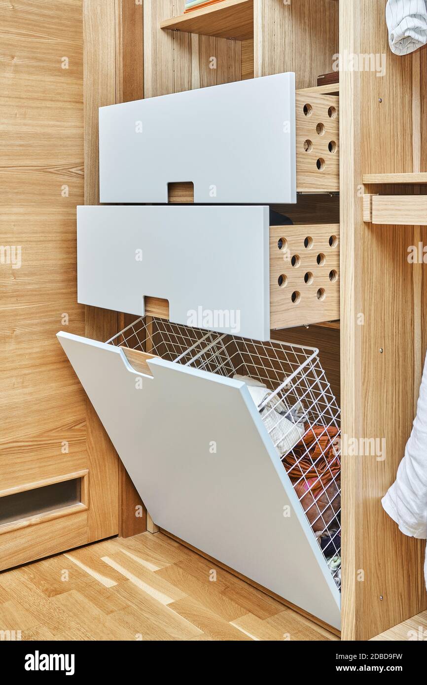 Modern wardrobe with opened metal mesh laundry basket and wooden drawers. Wooden wardrobe with