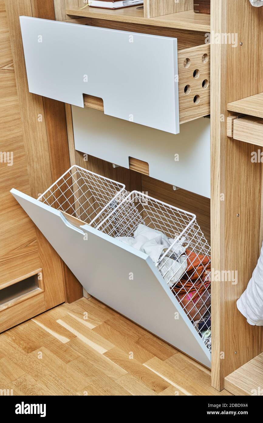 Modern wardrobe with opened metal mesh laundry basket and wooden drawers. Wooden wardrobe with