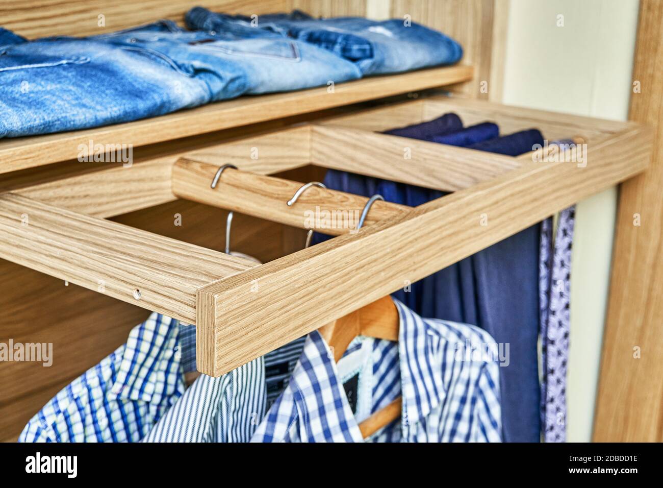 Internal details of the wooden wardrobe with slide out rack for coathangers. Modern wardrobe with clothes hanging on slide out racks and folded on the Stock Photo