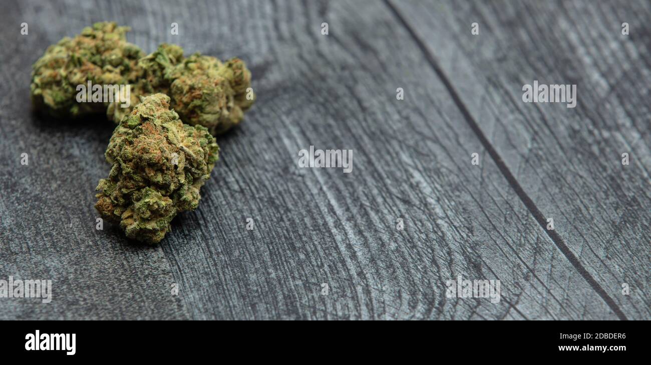 Three high quality bright green marijuana buds on a wooden table. Orange color and many crystals on buds. Stock Photo