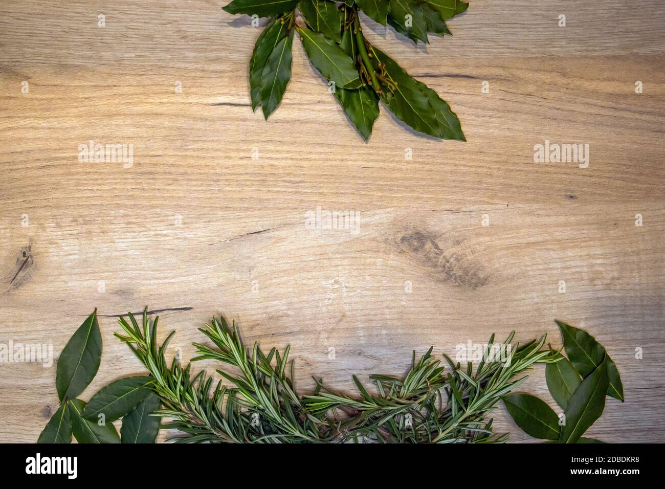 Light wooden board framed with fresh rosemary sprigs and bay leaves, design template Stock Photo