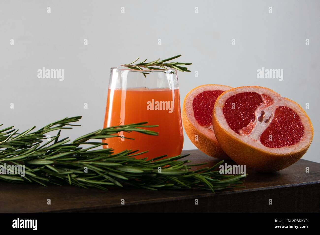 Two halves of red orange, rosemary sprig and glass of orange juice lying on a wooden table against light background Stock Photo