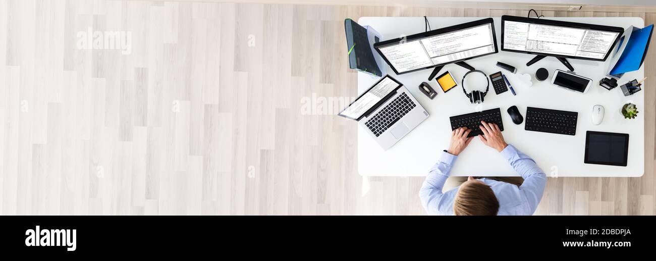 Developer Working On Multiple Computer Screens At Office Desk Stock Photo