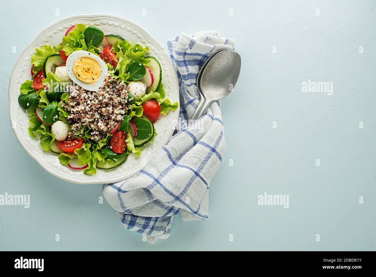 Healthy Green salad meal with quinoa seeds, egg and fresh vegetables on blue table background Stock Photo