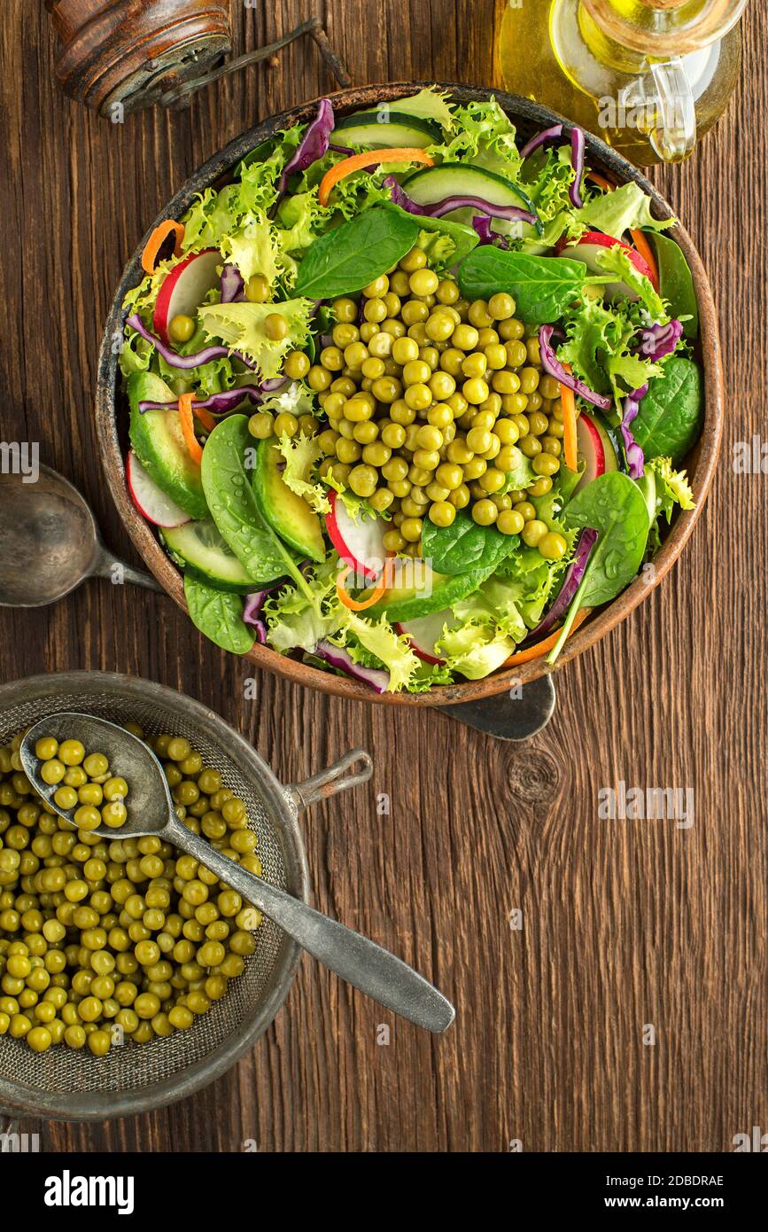 Green lettuce salad with fresh vegetables and cooked peas on wooden table background Stock Photo