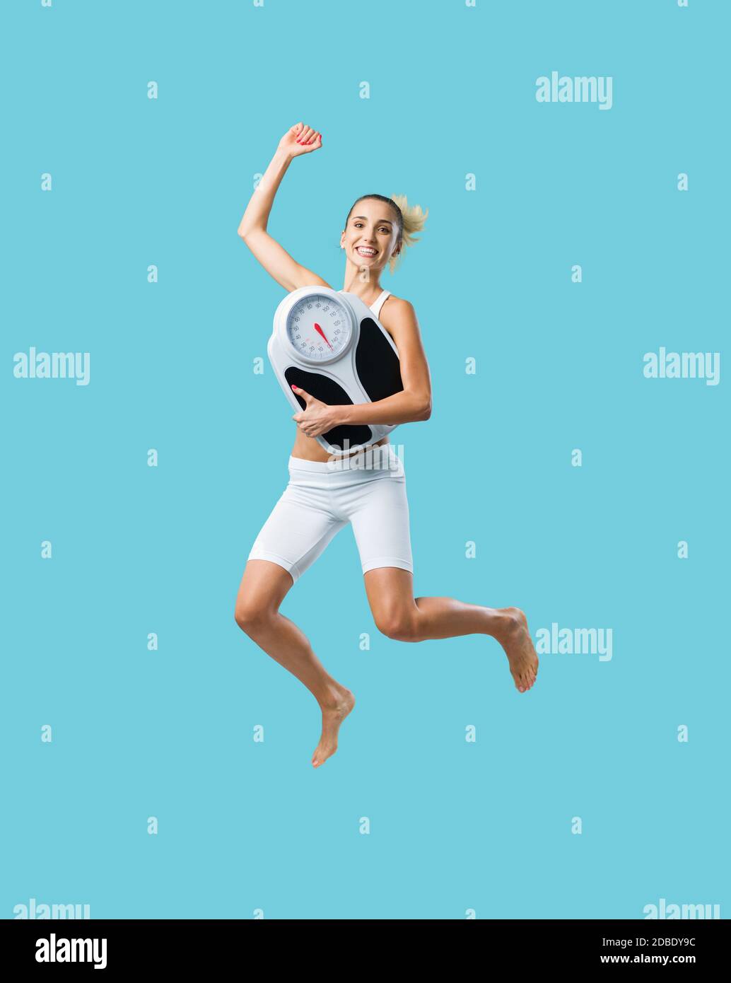Cheerful young woman jumping and holding a weight scale, weight loss and fitness concept Stock Photo