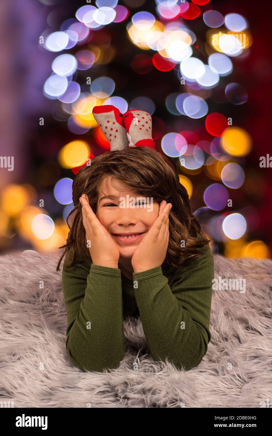 Cheerful boy laying on fluffy carpet in front of Christmas lights Stock
