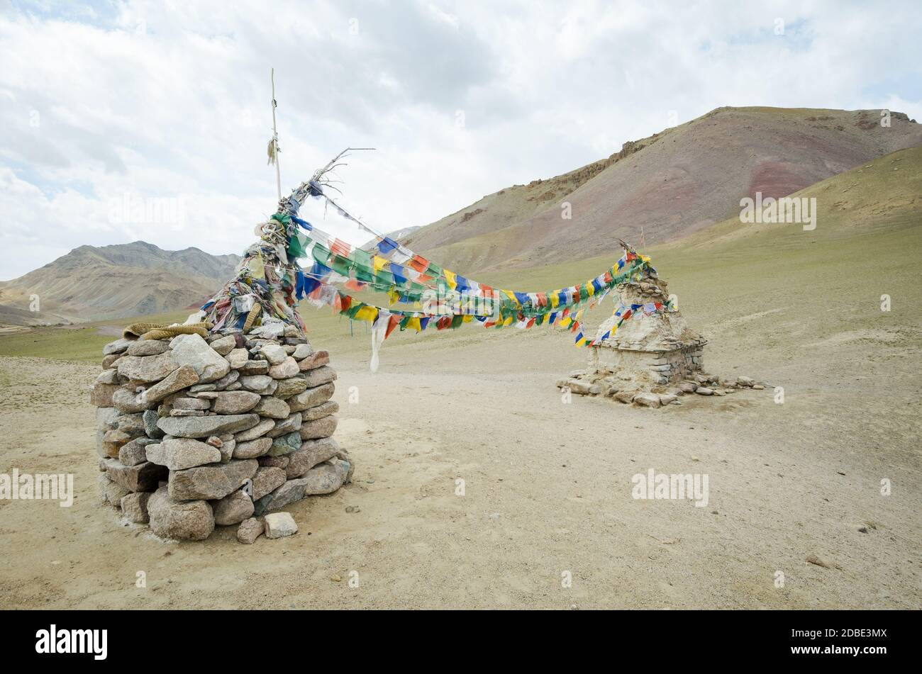 Milestone and Tibetan-style flags over a path in the Ladak mountain range, India Stock Photo