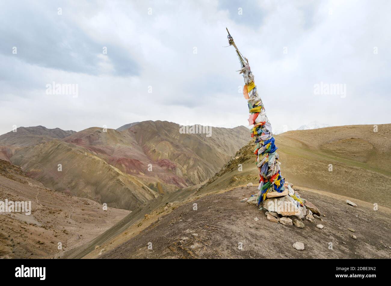 Flagpole covered with prayer flags to mark a hiking trail in the dry landscape of the Indian Himalayas, near Leh, Ladak, India Stock Photo