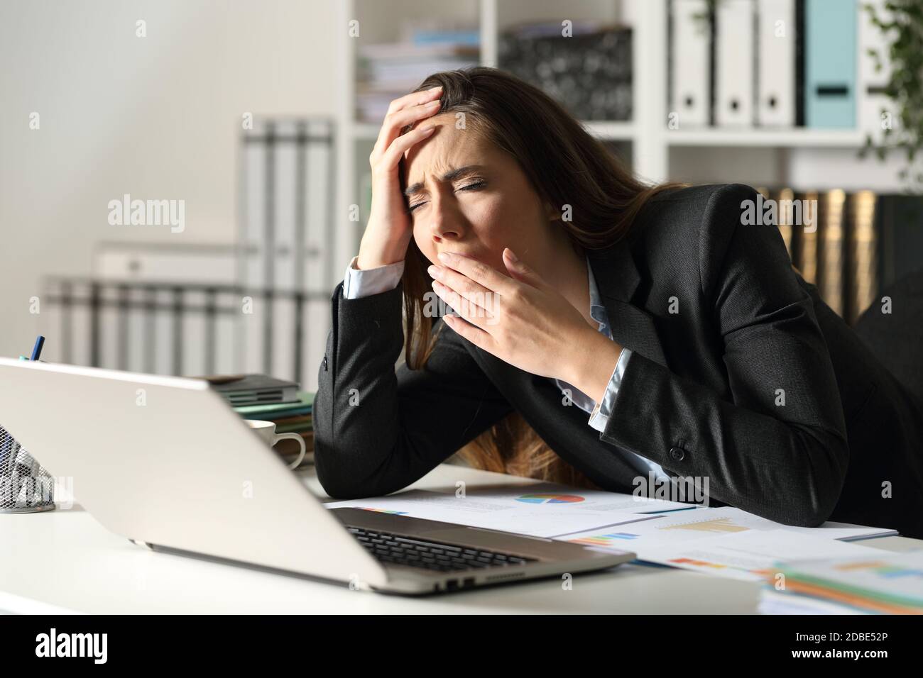 Tired executive woman yawning working late sitting on her desk at night ...