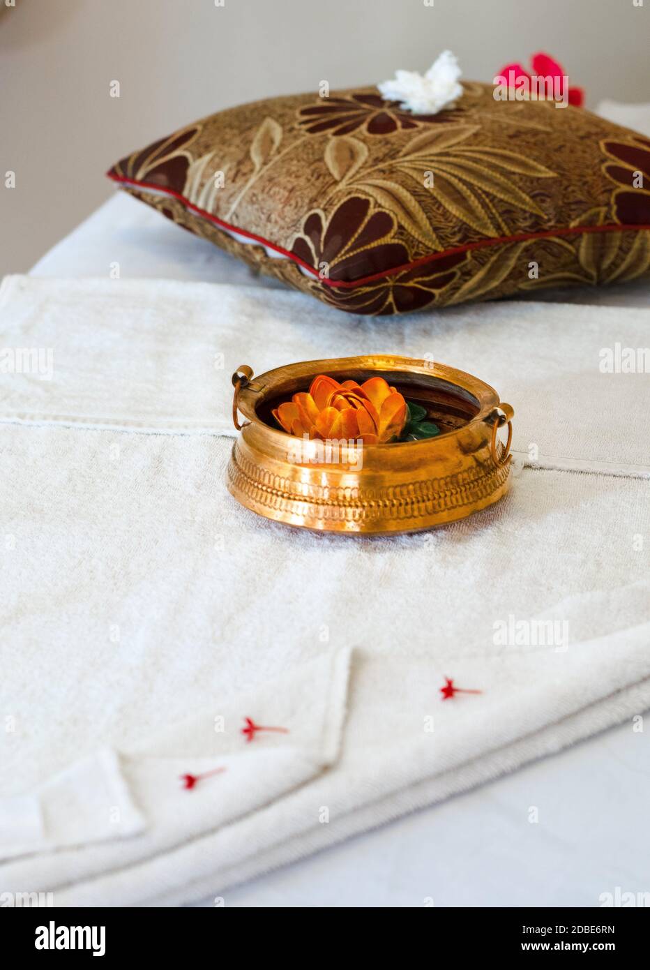 Luxury body massage set with folded towels, flower petals, pebble stones and copper containers on a massage bed Stock Photo