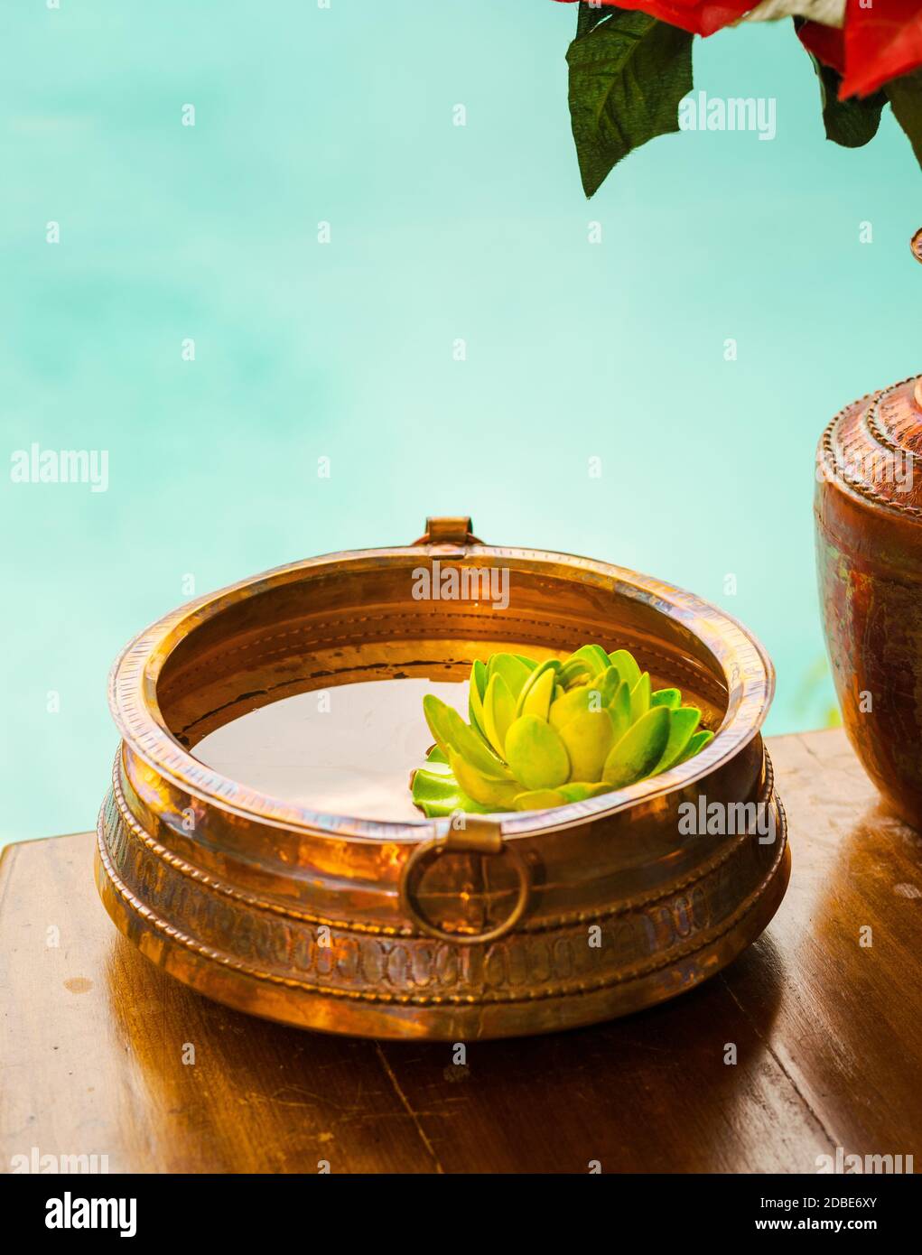 Copper recipient with water and lotus flower on a wooden deck next to a spa swimming pool, in a luxury massage resort, Nepal. Stock Photo