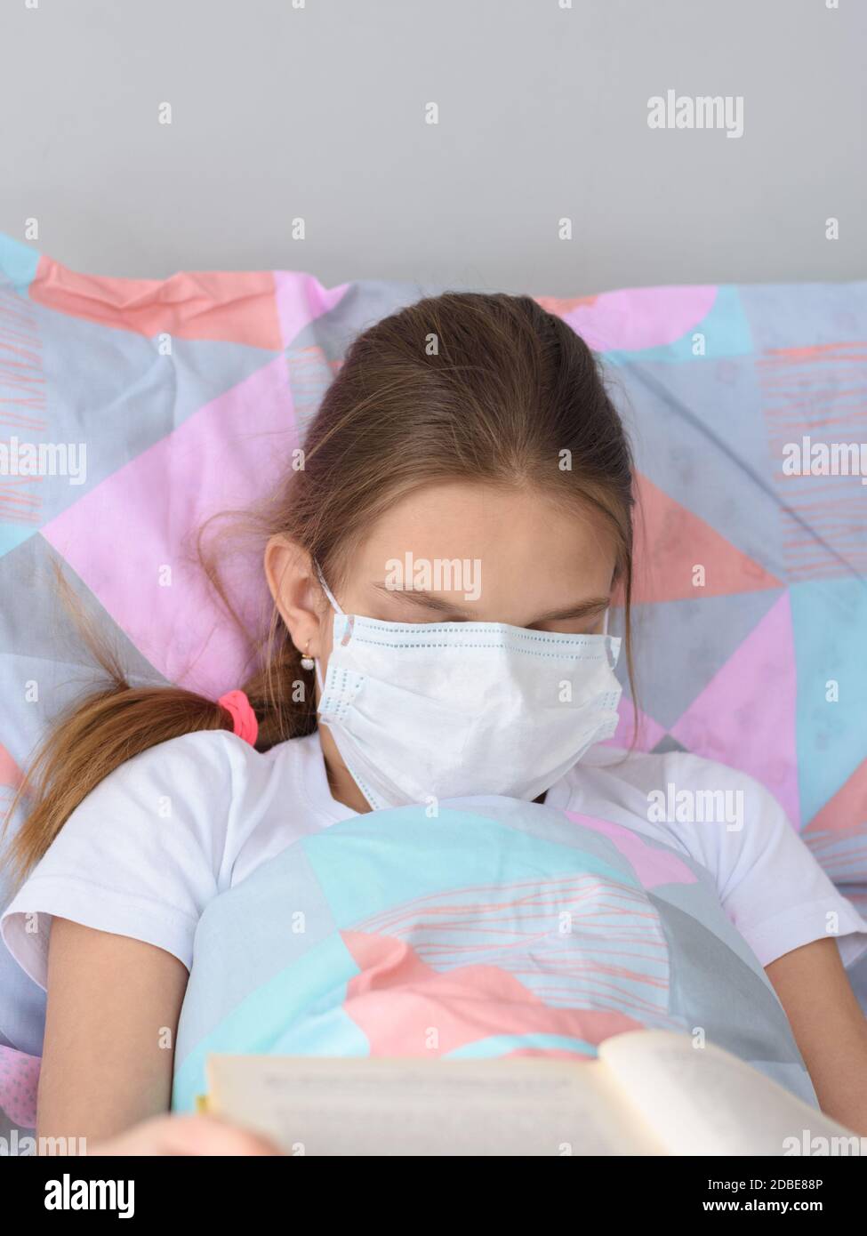 The sick girl decided to fall asleep while reading a book and pulled a medical mask over her face Stock Photo