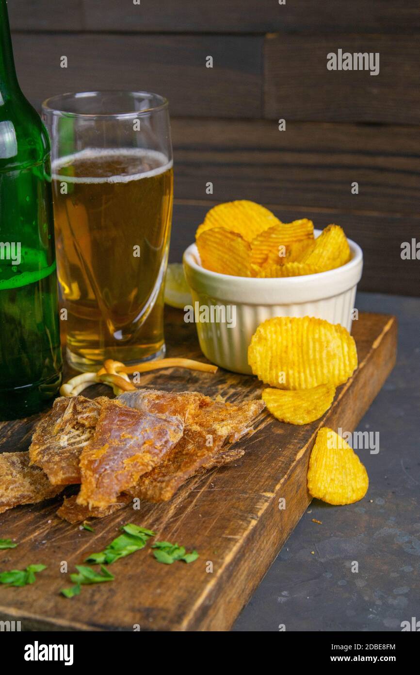 Dried cod with pepper with beer, lemon and potato chips on dark wooden
