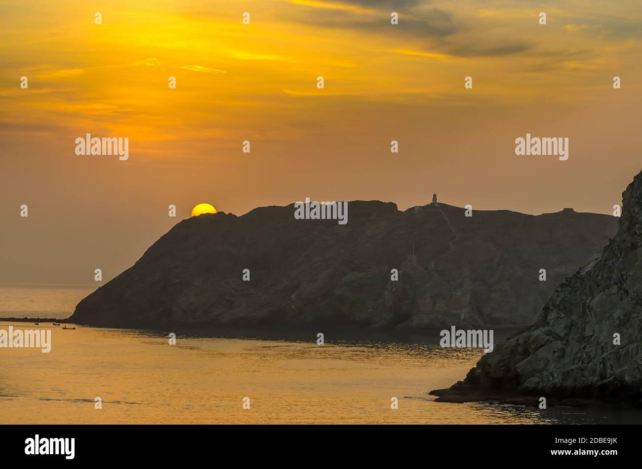 Golden Sun peeking out from behind a mountain with a golden sky background in Muscat, Oman. Stock Photo