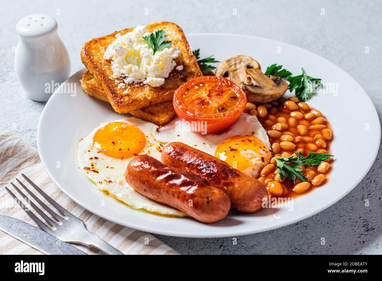 English breakfast with sausages, beans, fried eggs, toast, mushrooms and tomatoes in a white plate. English breakfast concept. Stock Photo