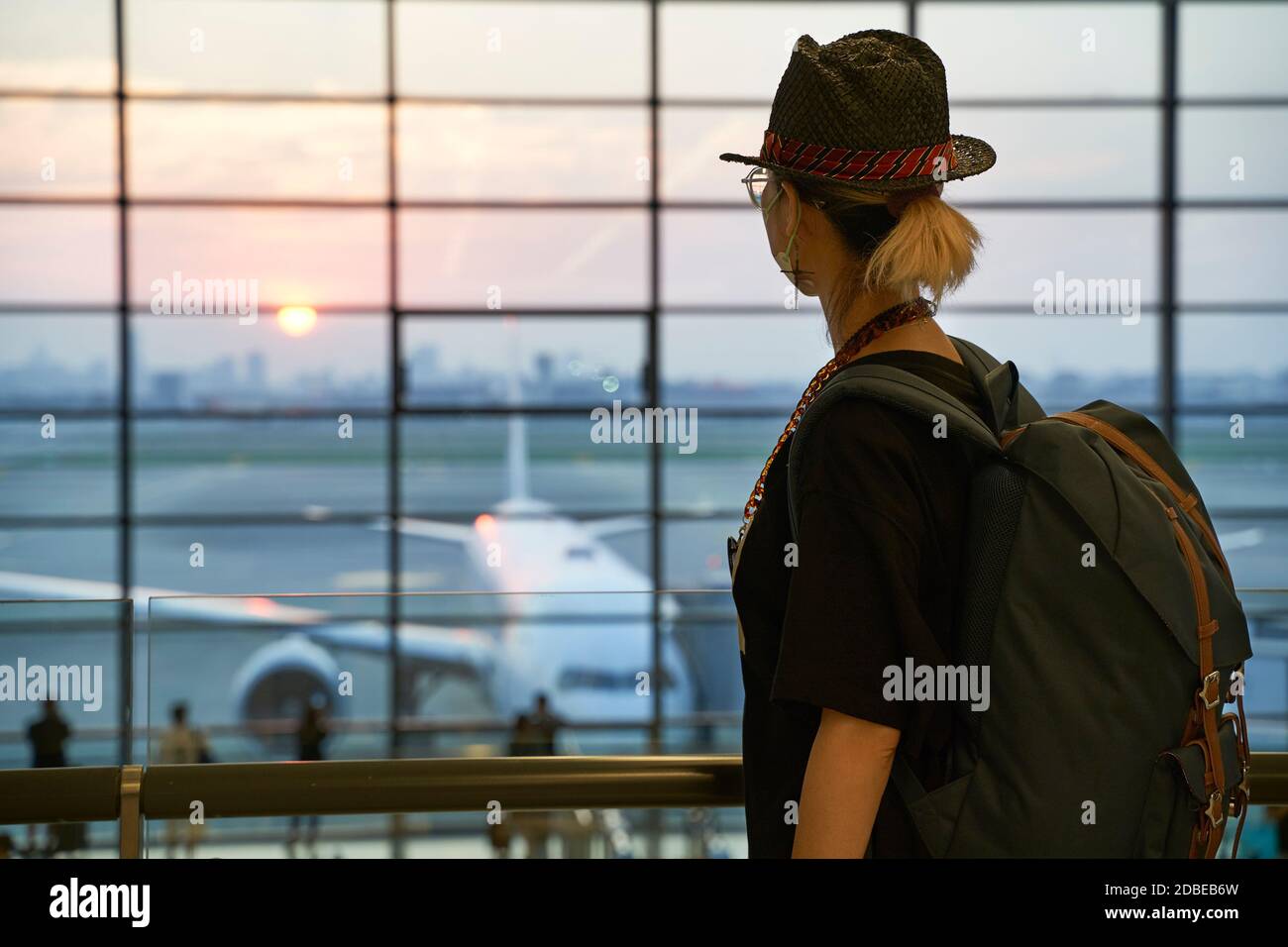 asian woman air traveler looking at sunrise through window while walking in airport terminal building Stock Photo