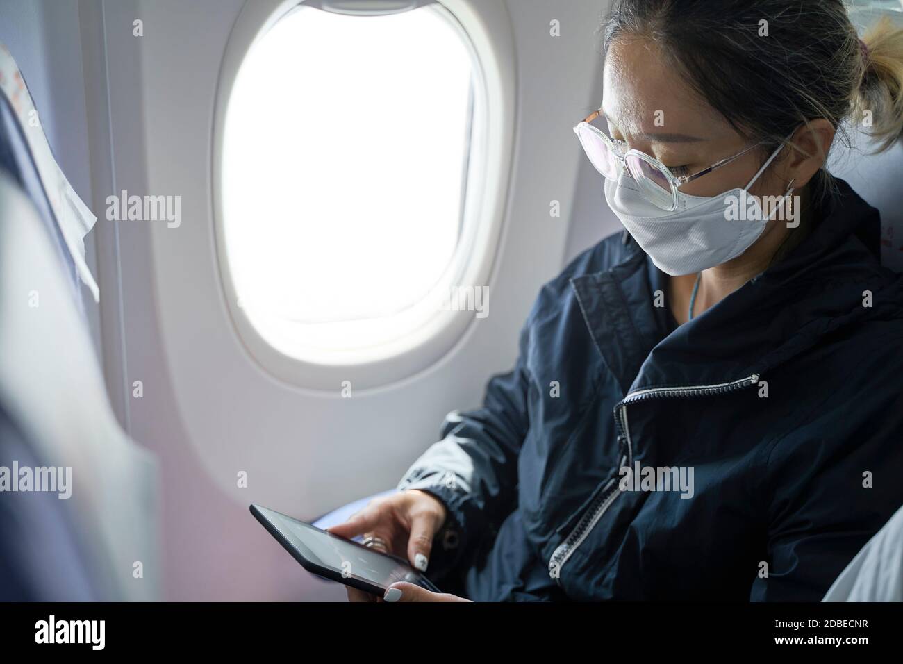 asian woman female passenger sitting in cabin of airplane reading ebook