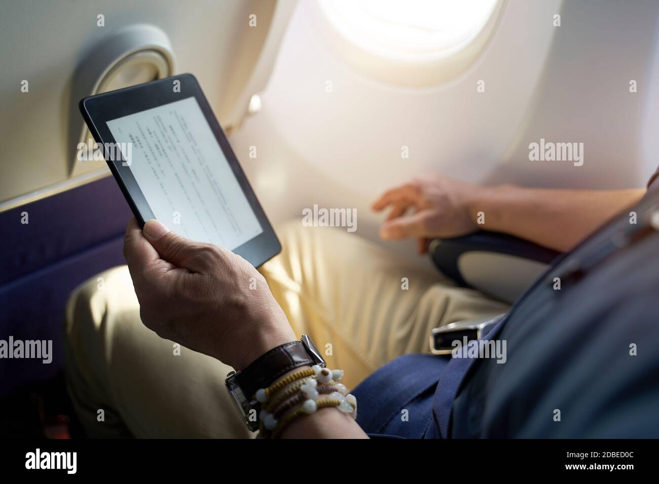 asian man male passenger sitting in cabin of airplane reading ebook using e-reader Stock Photo