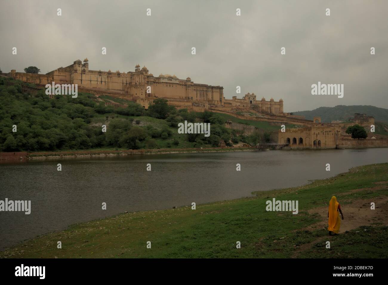 A woman in working dress walking on the side of Maota Lake, overlooking the historic Amer Fort in Amer, Rajasthan, India. Stock Photo