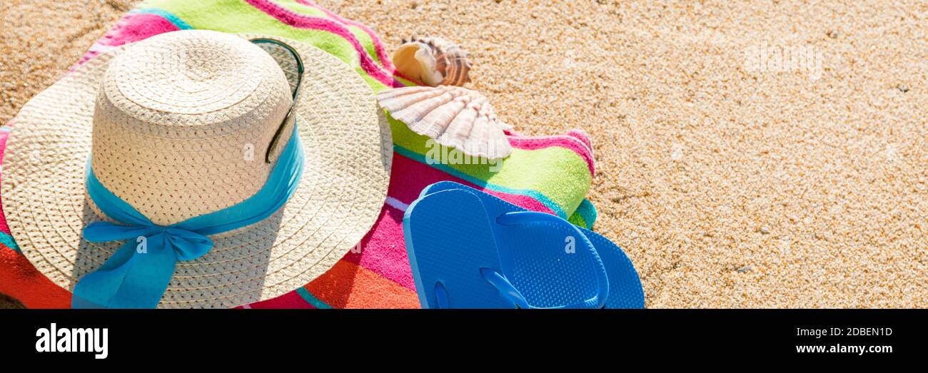 Beach towel with hat, sunglasses and flip flops photographed from above on sandy beach, hot summer day accessories, vacation destination, sunny tropical beach background Stock Photo