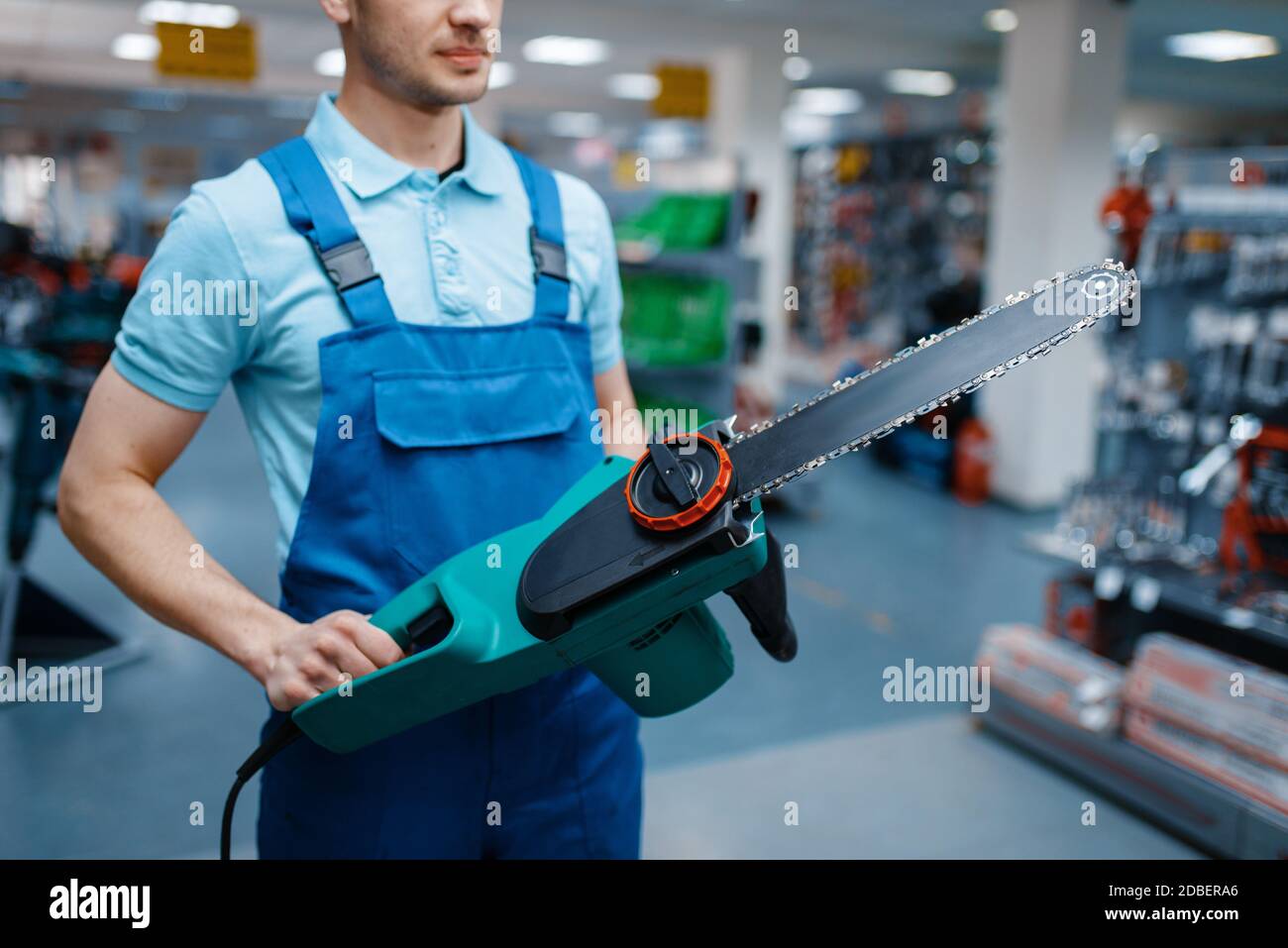 Male worker in uniform holds electric saw in tool store. Choice of professional equipment in hardware shop, instrument supermarket Stock Photo