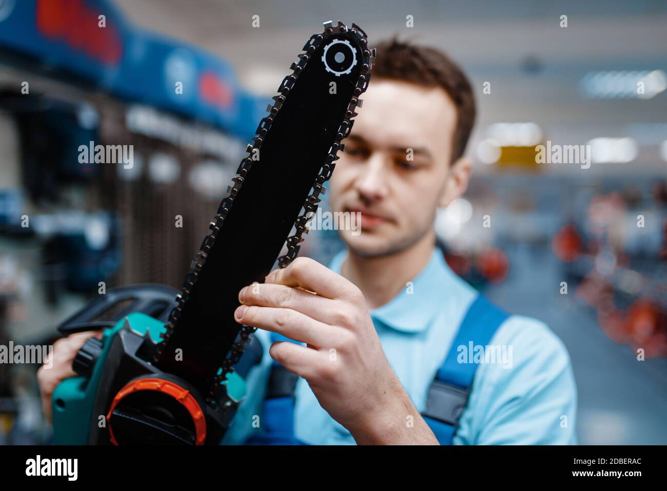 Male worker in uniform holds electric saw in tool store. Choice of professional equipment in hardware shop Stock Photo