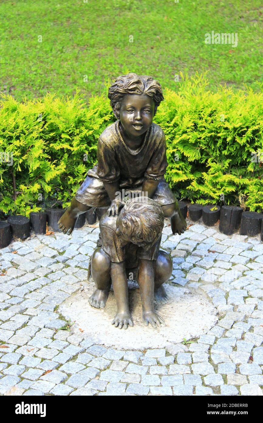 Bronze sculpture of children playing leapfrog in summer park. Boy and girl playing leapfrog in park. Sculpture children make leapfrog in city park of Stock Photo