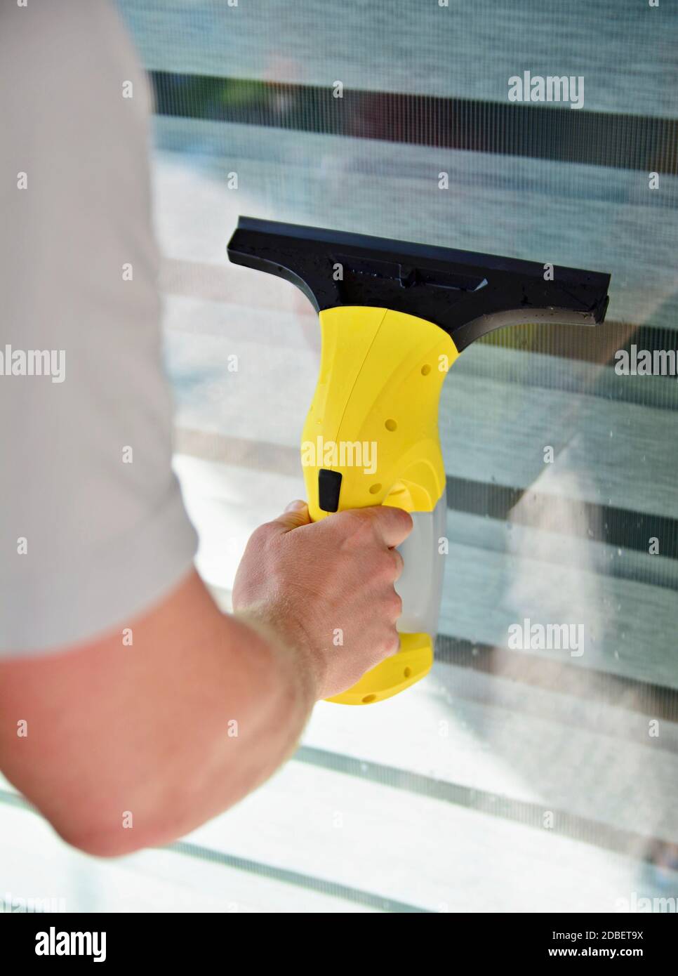 Cleaning window with cordless electrical vacuum cleaner. Man holding and using vacuum cleaner