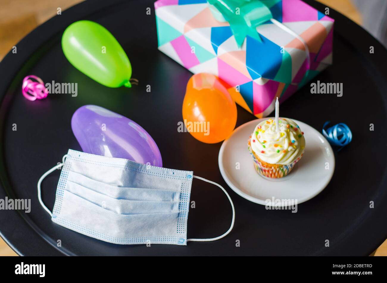 Quarantine birthday in isolation. Birthday cupcake with candle, face mask, gifts and holiday accessories. Social distance. Stock Photo