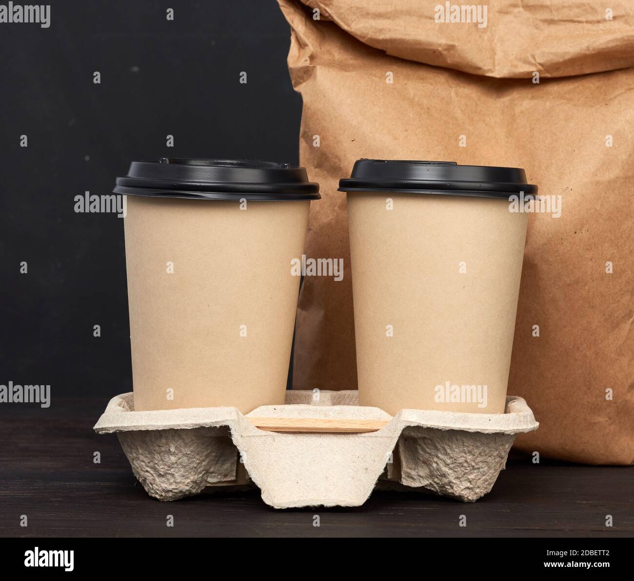 https://c8.alamy.com/comp/2DBETT2/brown-paper-disposable-cups-with-a-plastic-lid-stand-in-the-tray-on-a-wooden-table-black-background-takeaway-containers-2DBETT2.jpg