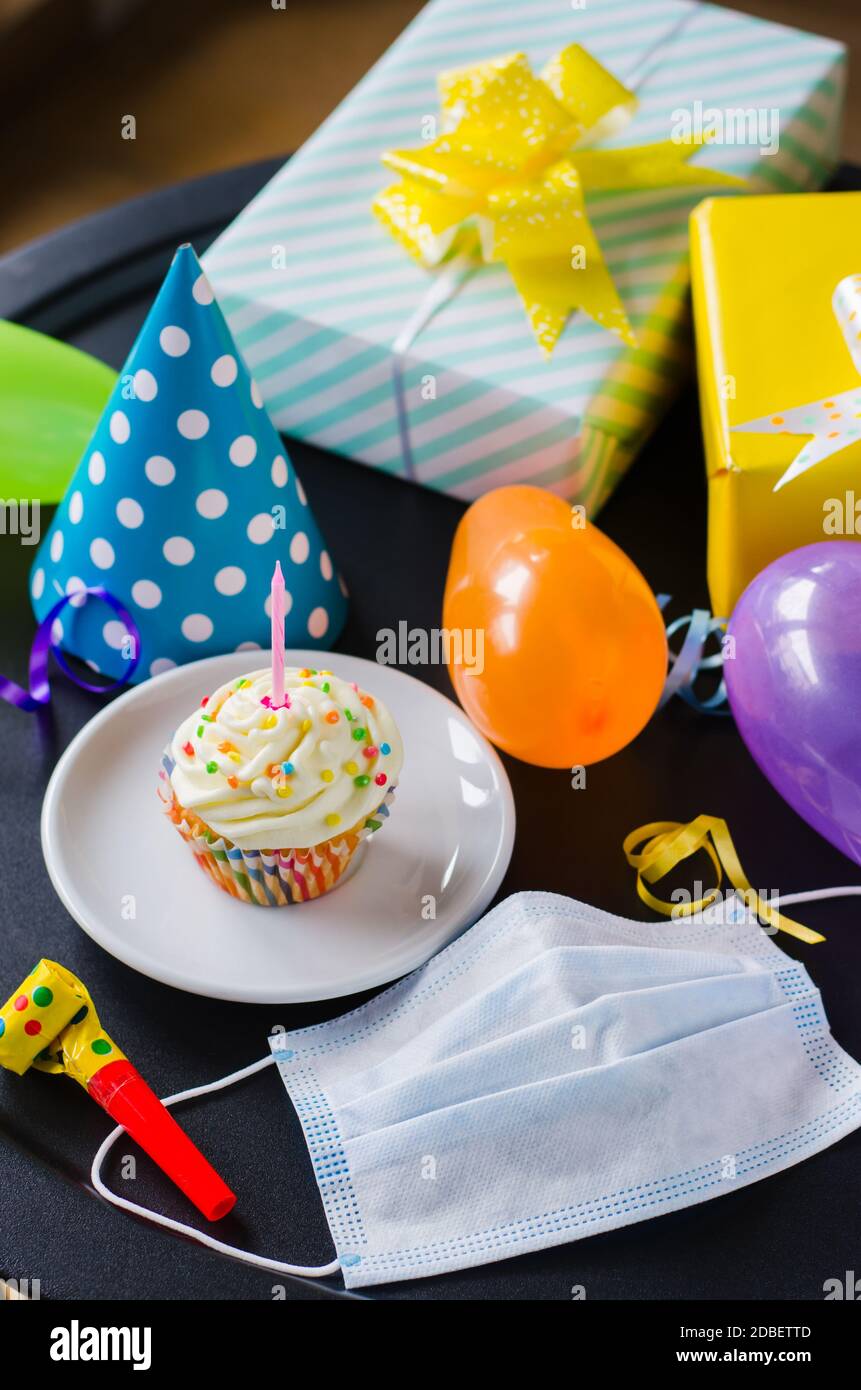 Quarantine birthday in isolation. Birthday cupcake with candle, face mask, gifts and holiday accessories. Social distance. Stock Photo