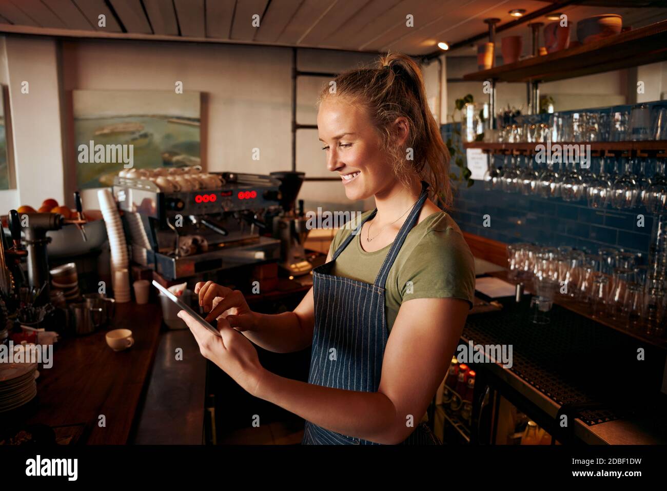 Young female staff wearing apron working with a digital tablet at the counter of cafe Stock Photo