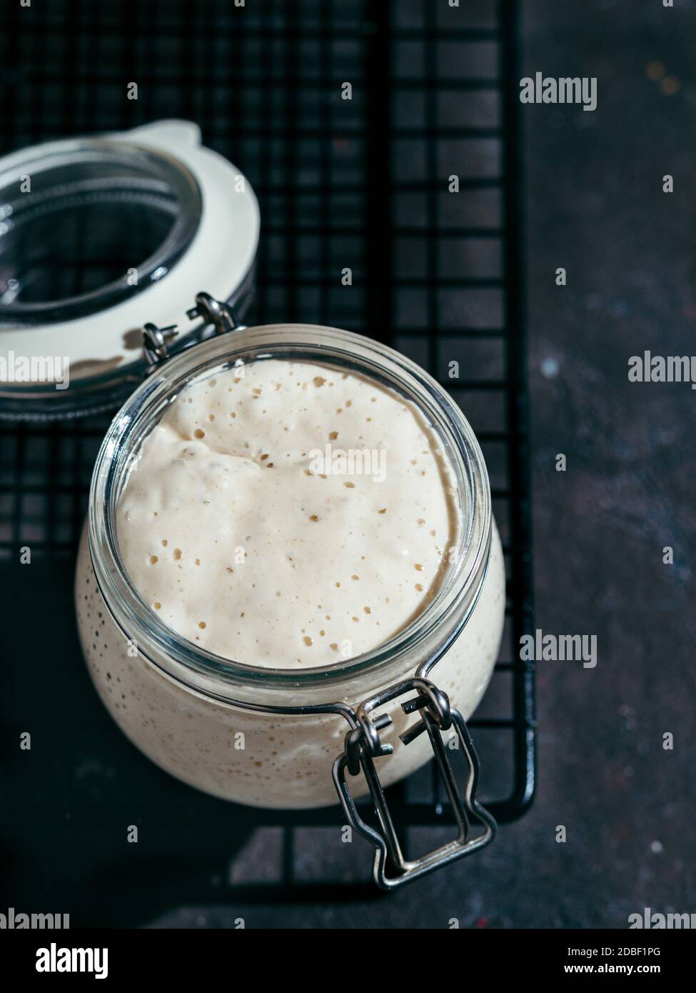Wheat sourdough starter. Glass jar with sourdough starter on dark