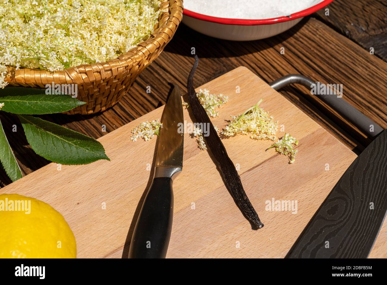 On a cutting board lies a kitchen knife and a vanilla pod as ingredients for the elderflower liqueur Stock Photo