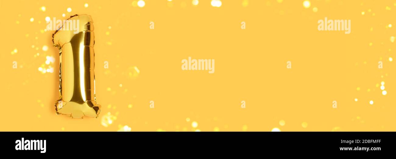 Banner with number 1 golden balloon with shiny bokeh. One year anniversary celebration concept on a yellow background with place for text. Stock Photo