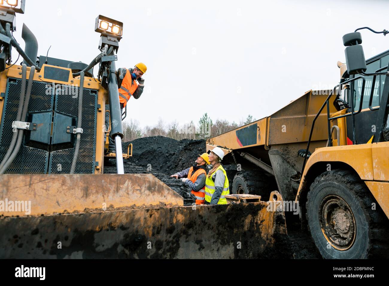Heavy machinery and workers in pit of quarry shouting at each other because the noise is unbearable Stock Photo