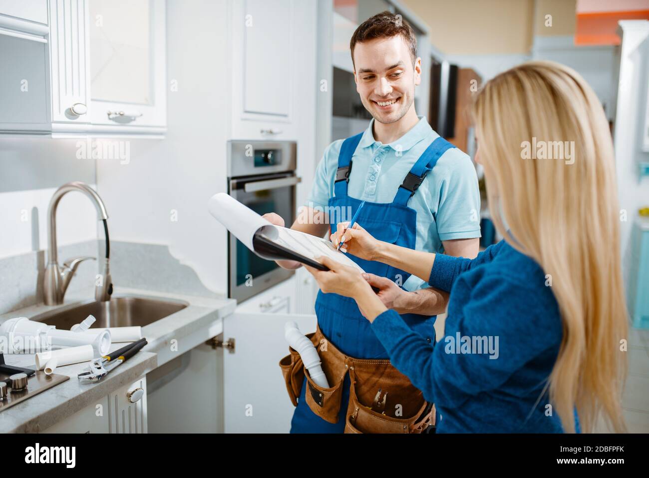 Male plumber in uniform and female customer in the kitchen. Handyman