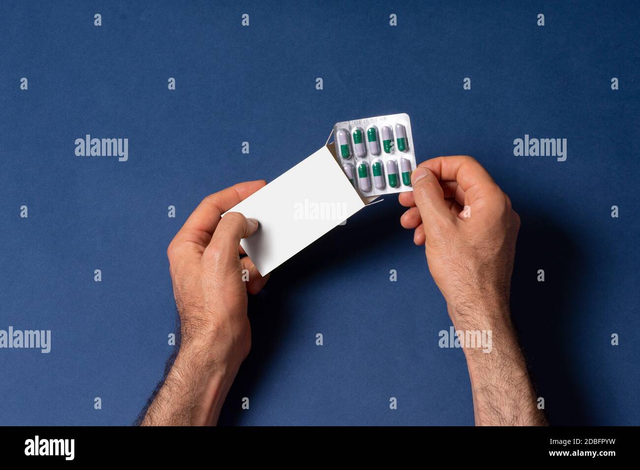 Male hand putting a capsule pills tablet in box in front of blue background, mock-up series template ready for your design, cover selection path inclu Stock Photo