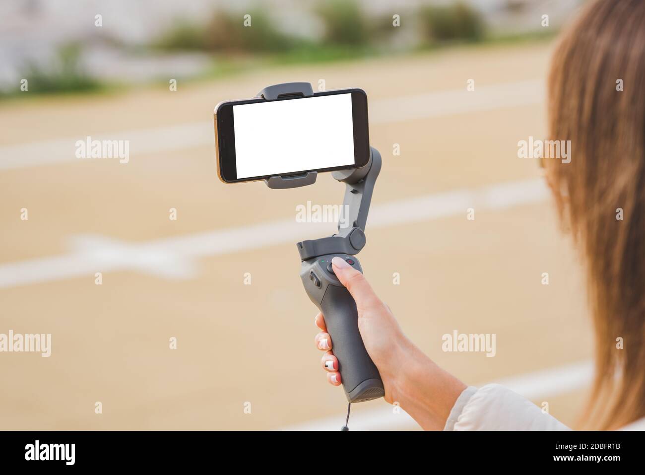 Woman hand holding gimbal with smartphone, blank screen. Taking pictures and live video. Vlog and video blogging concept Stock Photo