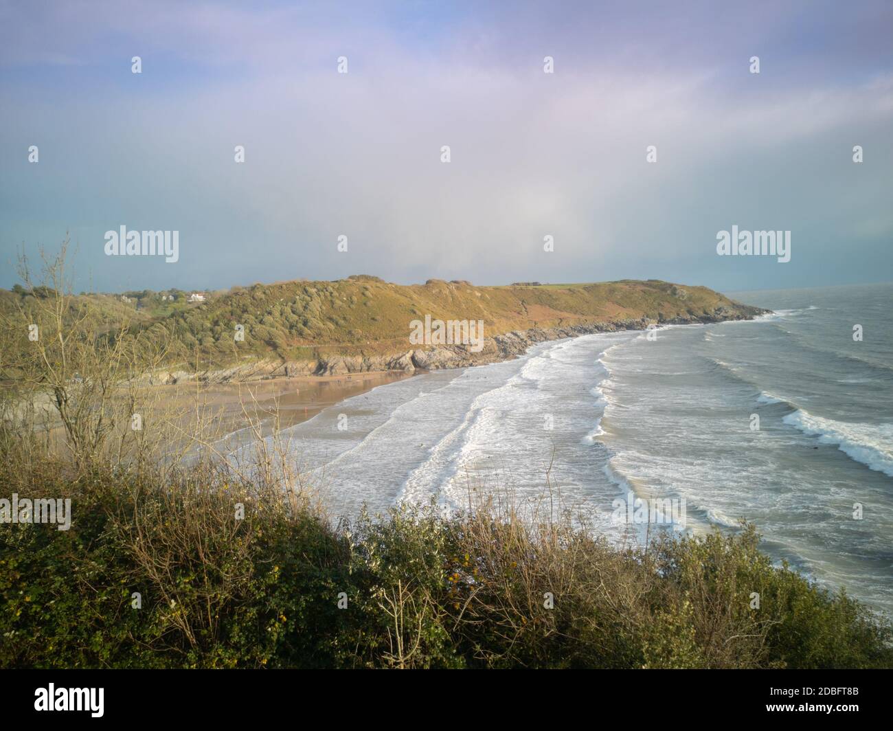 Approaching high-tide at Caswell Bay Beach in Wales, UK. Stunning view of crashing waves onto the sandy shores from the Gower Coastal Path towards sun Stock Photo